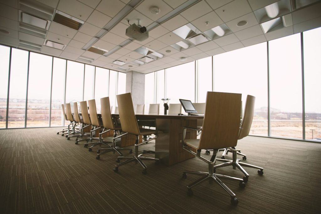 A quiet boardroom with an orderly conference table and chairs beside floor-to-ceiling windows.